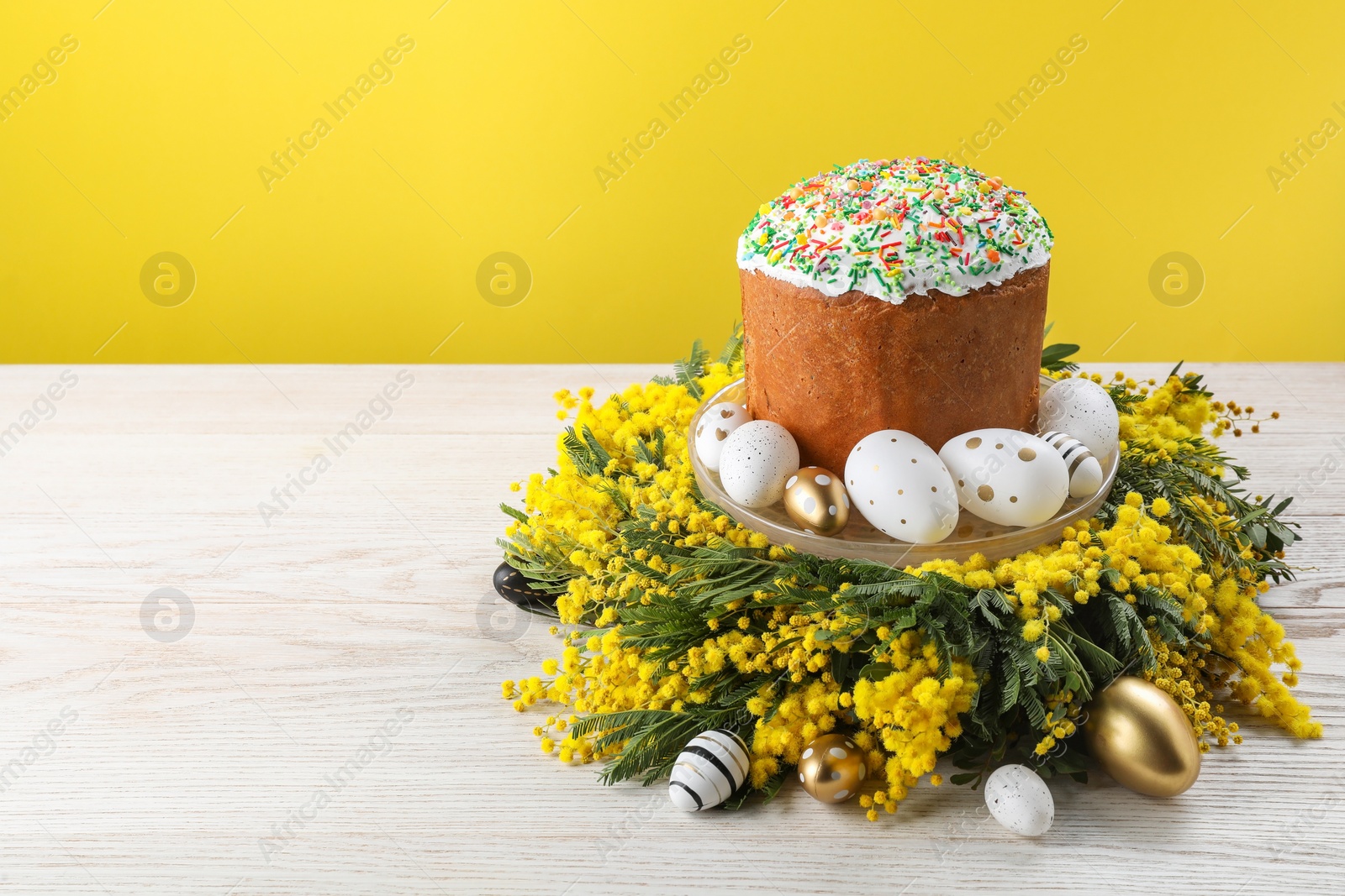 Photo of Traditional Easter cake with sprinkles, painted eggs and beautiful spring flowers on white wooden table, space for text