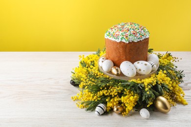 Traditional Easter cake with sprinkles, painted eggs and beautiful spring flowers on white wooden table, space for text