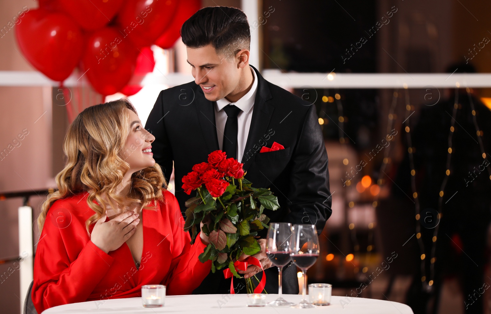 Photo of Man presenting roses to his beloved woman in restaurant at Valentine's day dinner