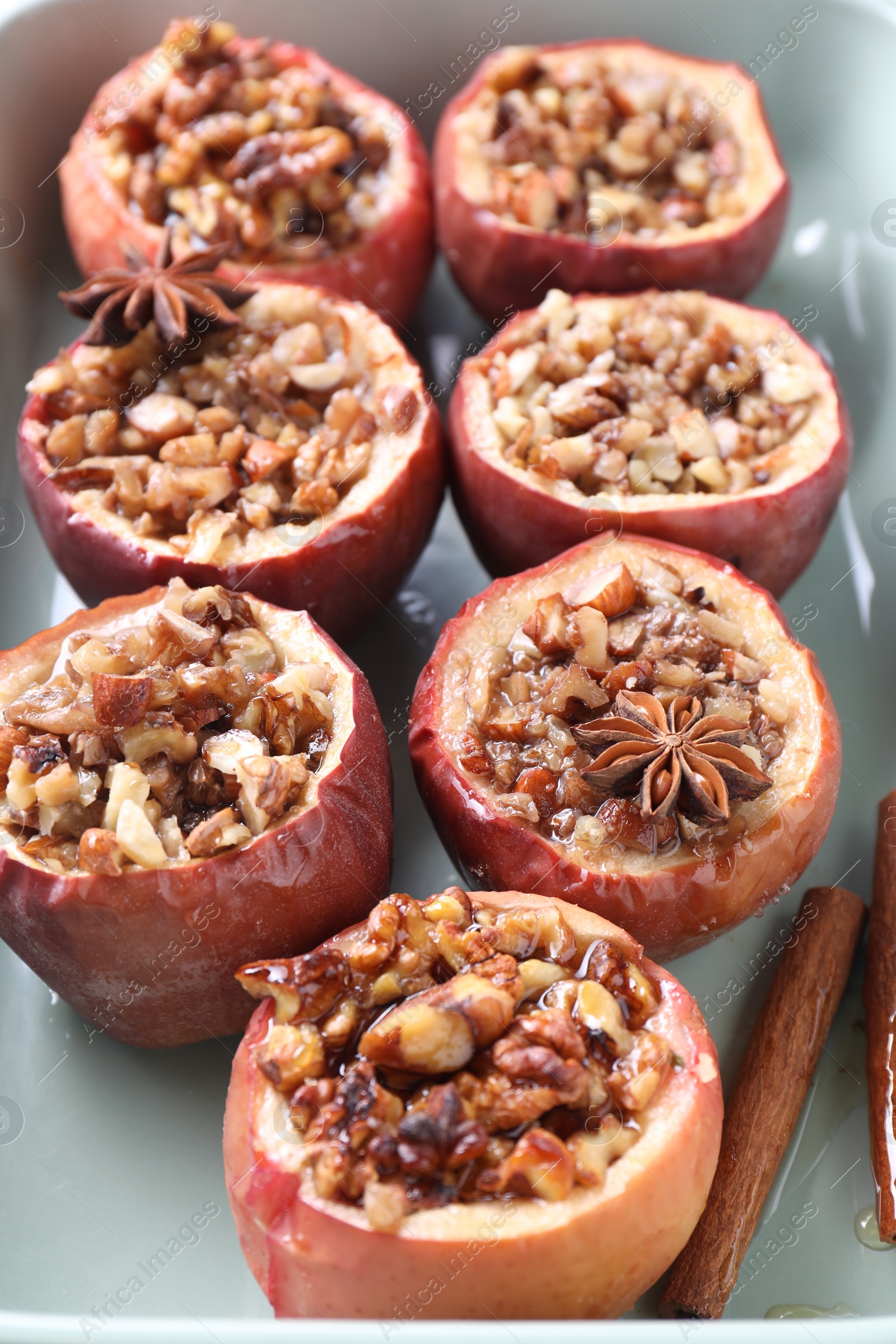 Photo of Tasty baked apples with nuts, honey and spices in dish, closeup