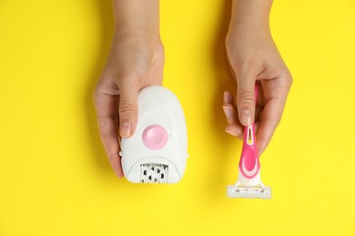 Woman holding modern epilator and razor on yellow background, top view