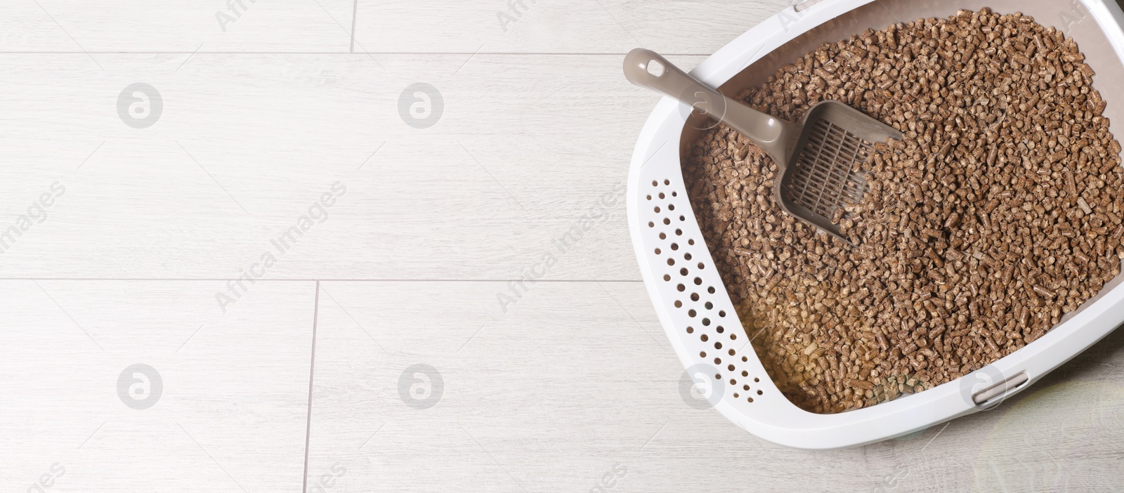 Image of Cat tray with biodegradable litter and scoop on wooden floor, top view. Banner design with space for text