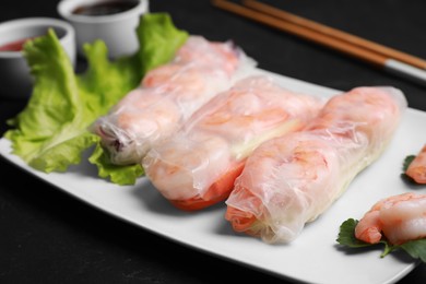 Photo of Delicious spring rolls with shrimps wrapped in rice paper served on black table, closeup