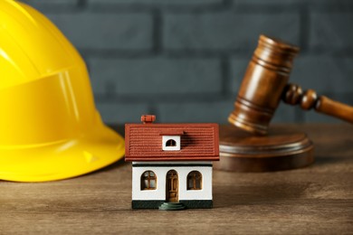 Photo of Construction and land law concepts. House model, gavel and hard hat on wooden table, closeup