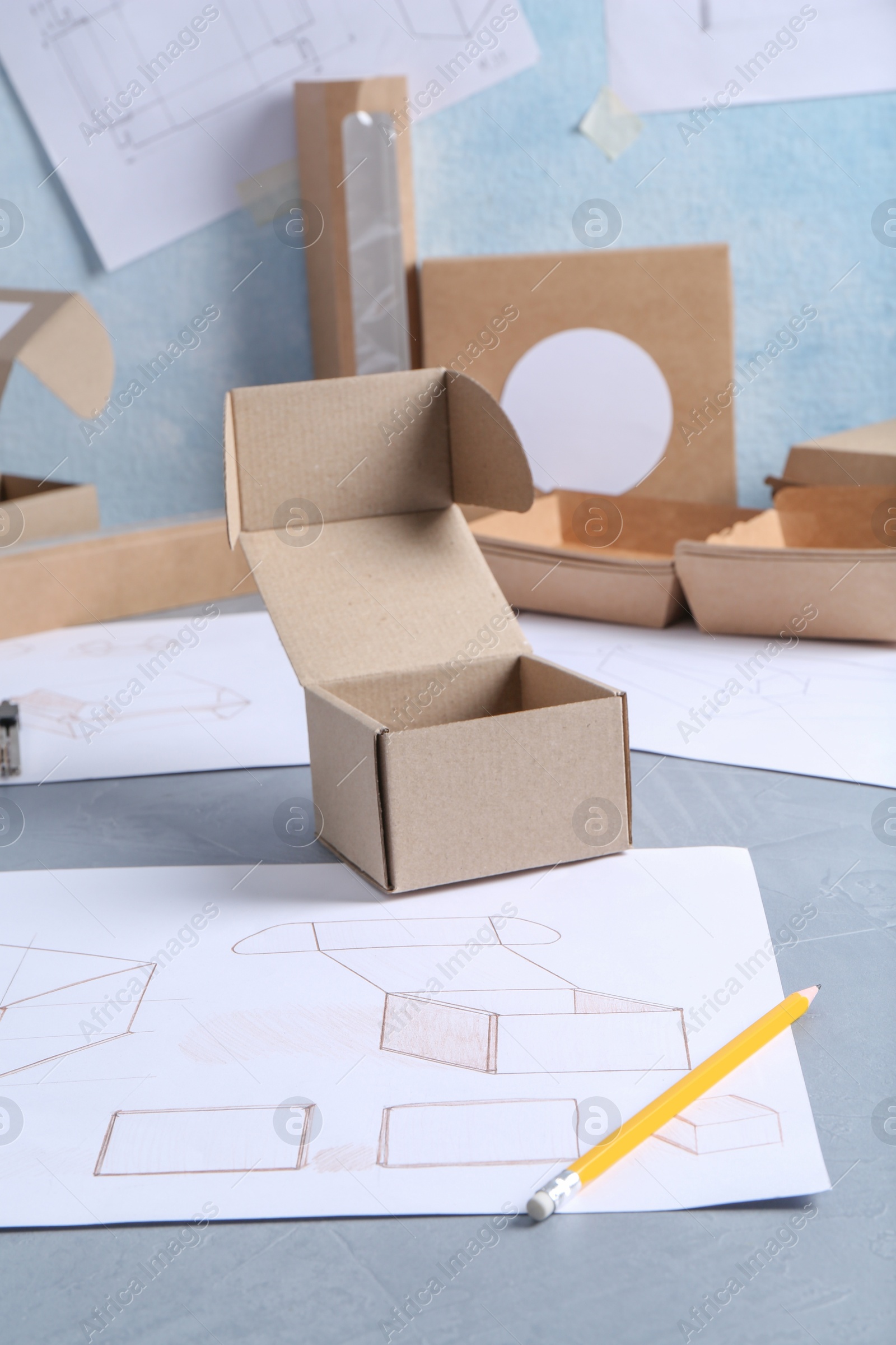 Photo of Creating packaging design. Drawings, boxes and pencil on blue textured table, closeup