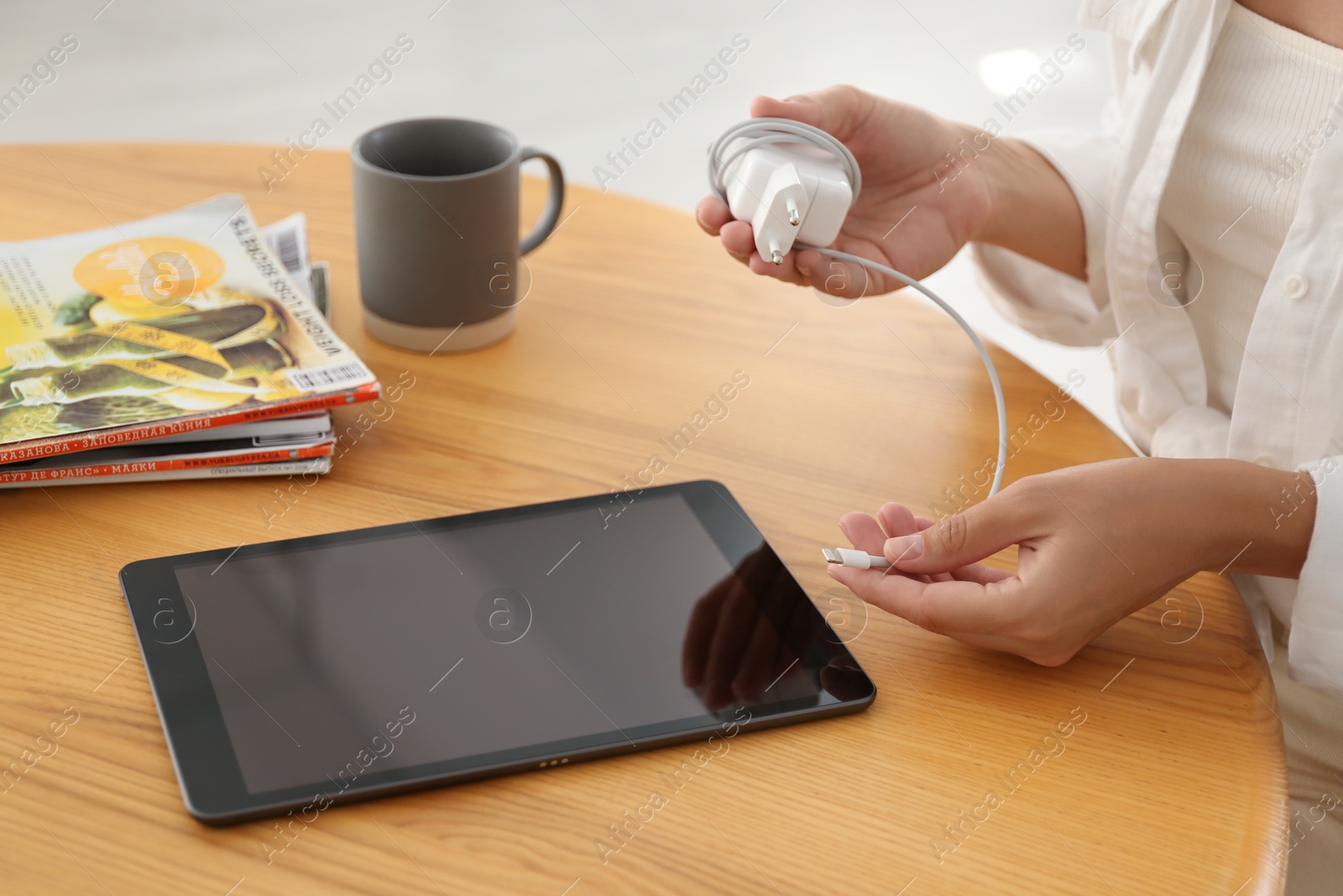 Photo of Woman connecting charger cable to tablet at wooden table, closeup