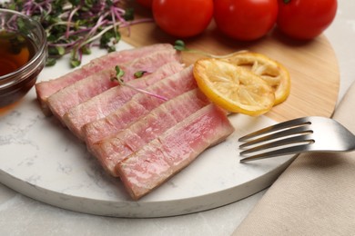 Photo of Pieces of delicious tuna steak with microgreens and lemon on table, closeup