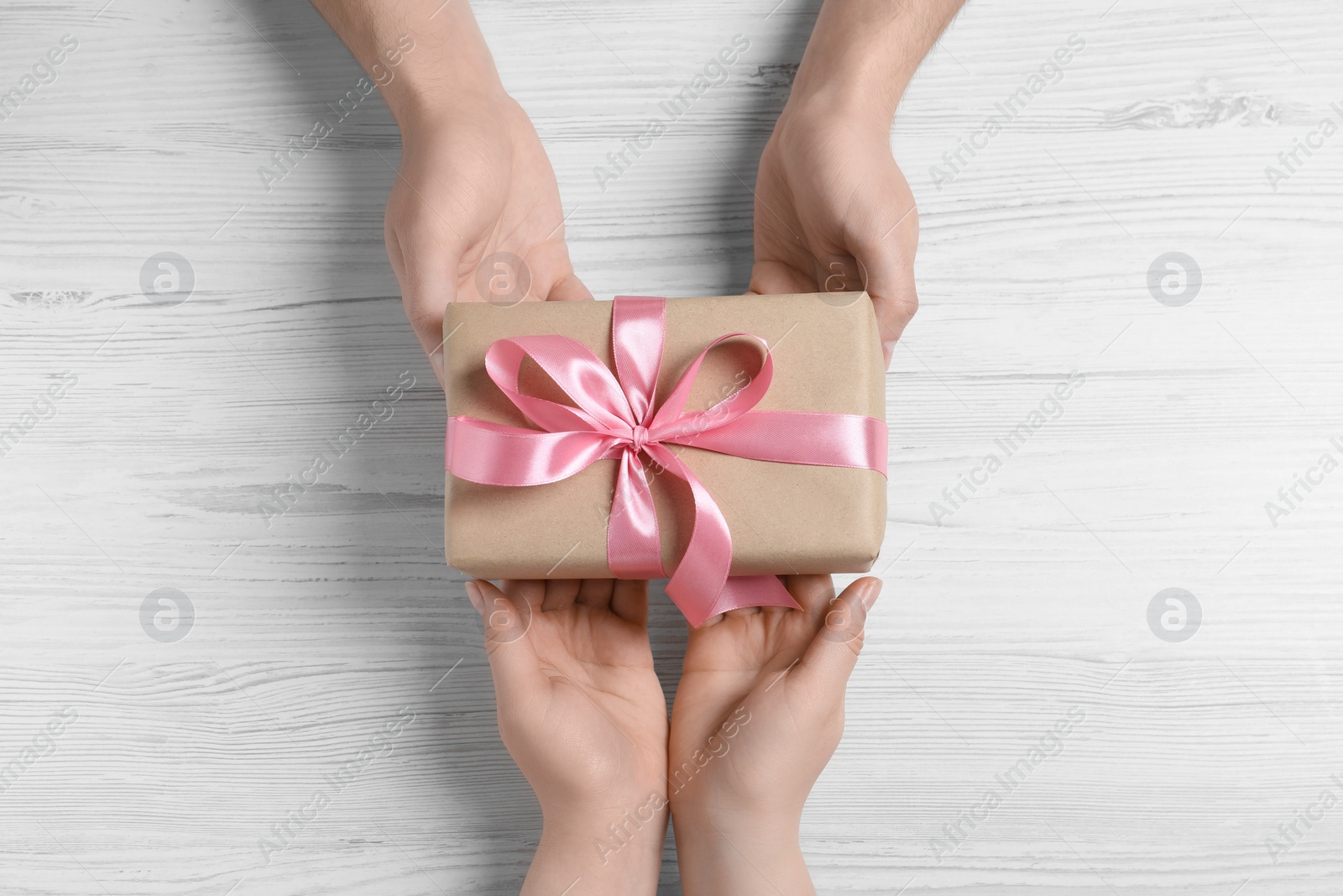 Photo of Man giving gift box to woman on white wooden table, top view