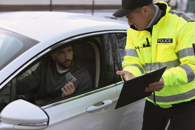 Photo of Man giving bribe to police officer out of car window outdoors