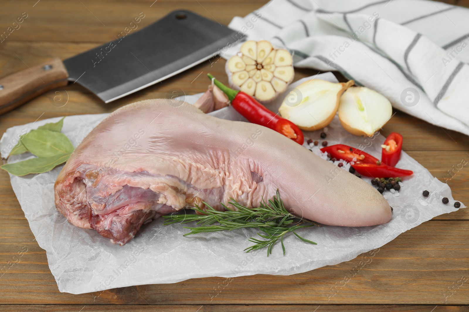 Photo of Parchment with raw beef tongue and products on wooden table, closeup