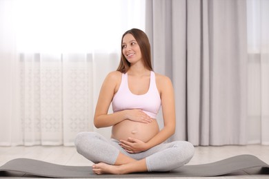 Photo of Pregnant woman sitting on yoga mat at home