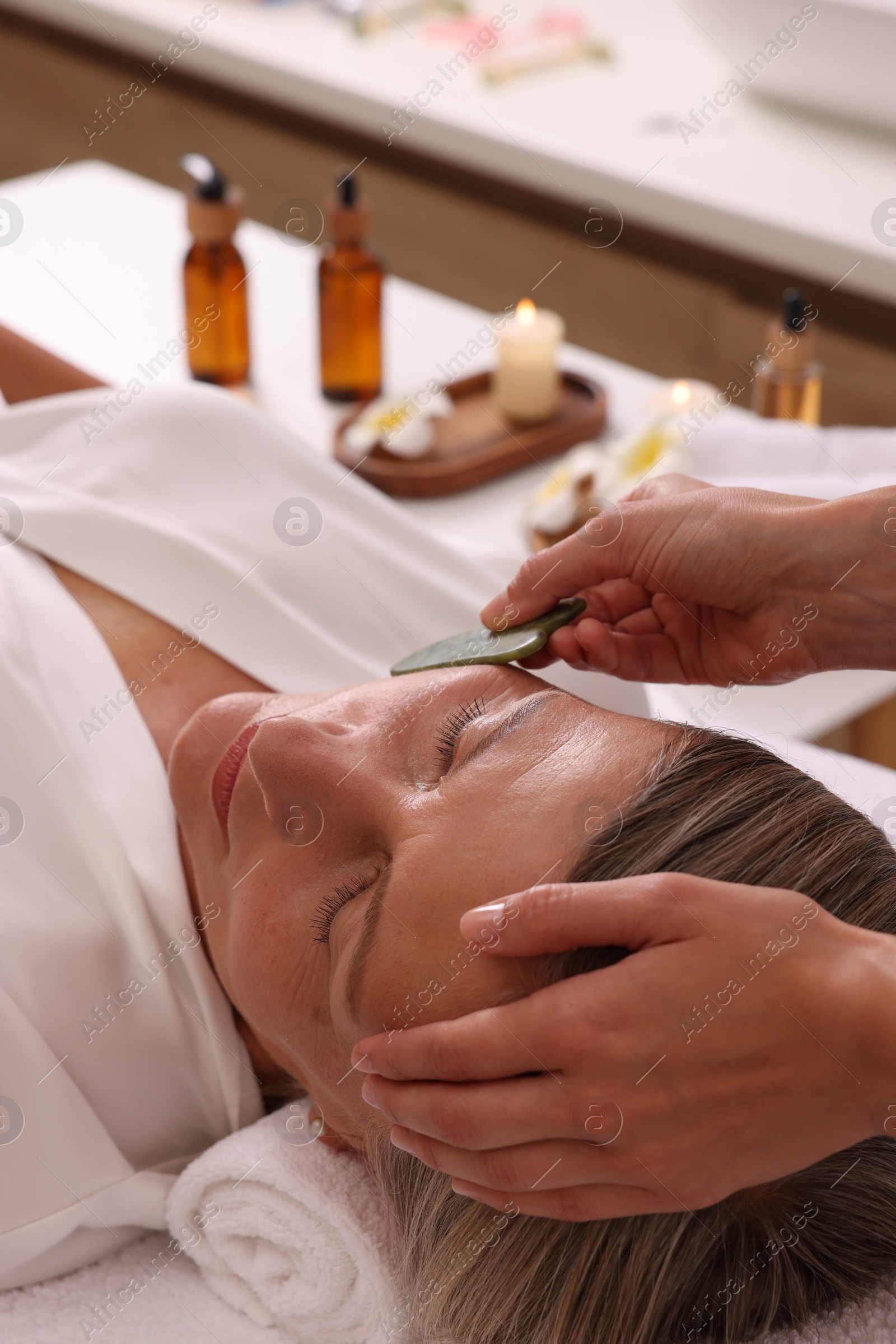 Photo of Woman receiving facial massage with jade gua sha tool in beauty salon, closeup