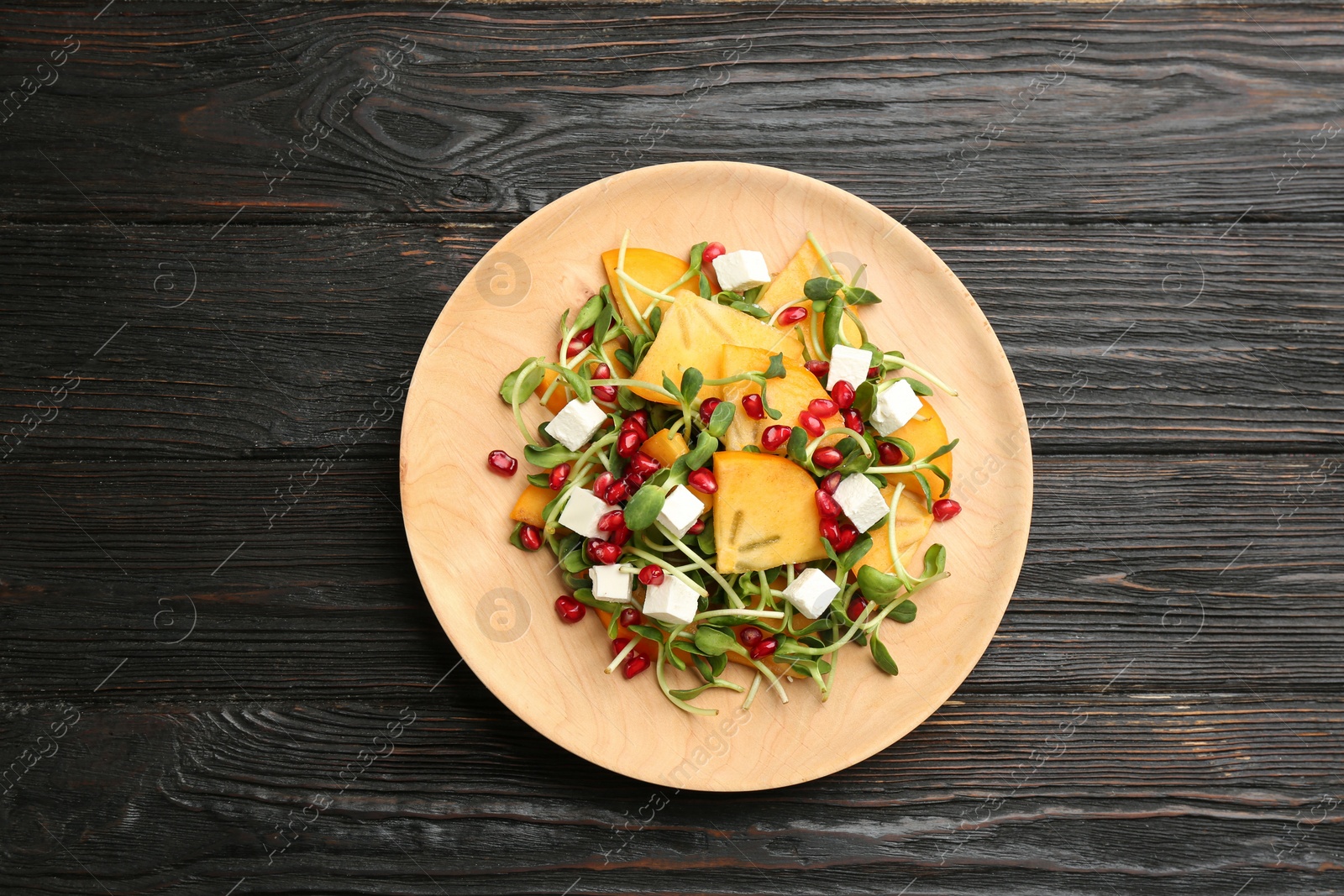 Photo of Delicious persimmon salad with pomegranate and feta cheese on wooden table, top view