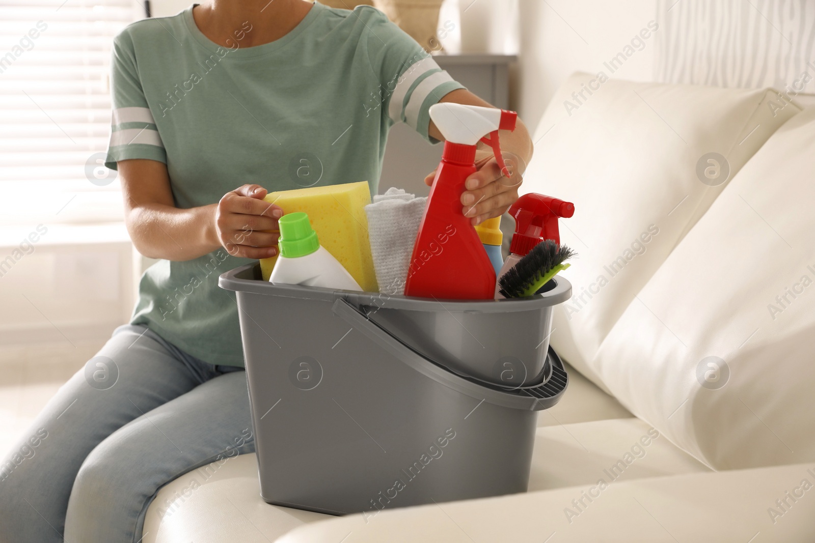 Photo of Woman holding bucket with cleaning supplies in living room, closeup