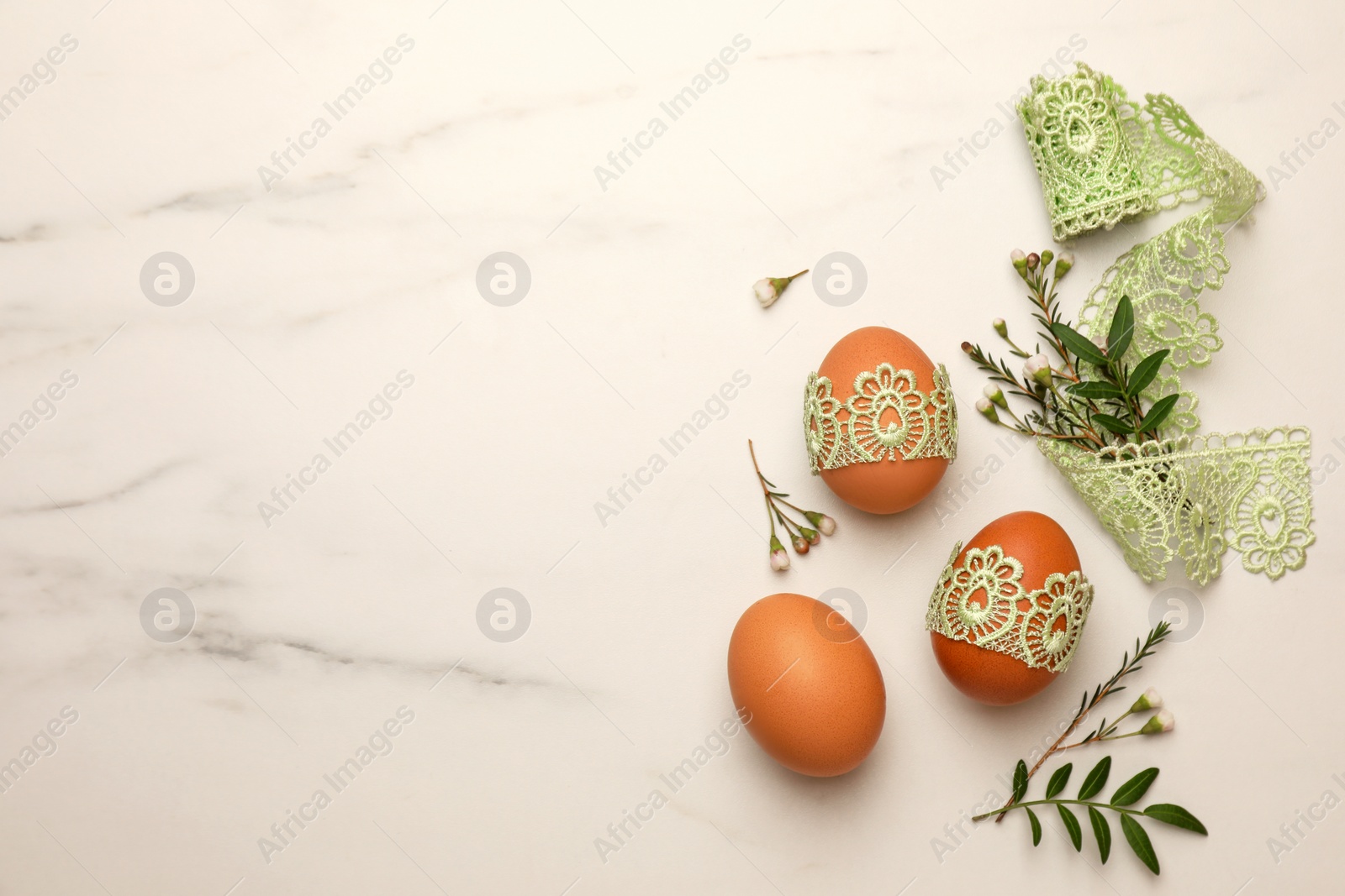 Photo of Flat lay composition with Easter eggs, twigs and lace ribbon on white marble table. Space for text