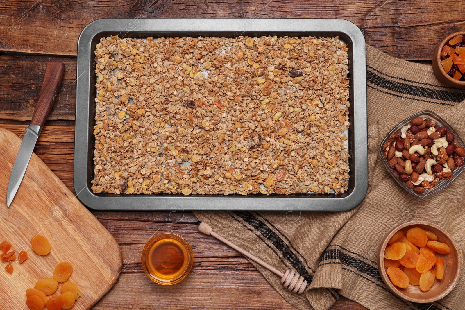 Photo of Making granola. Baking tray with mixture of oat flakes and other ingredients on wooden table, flat lay