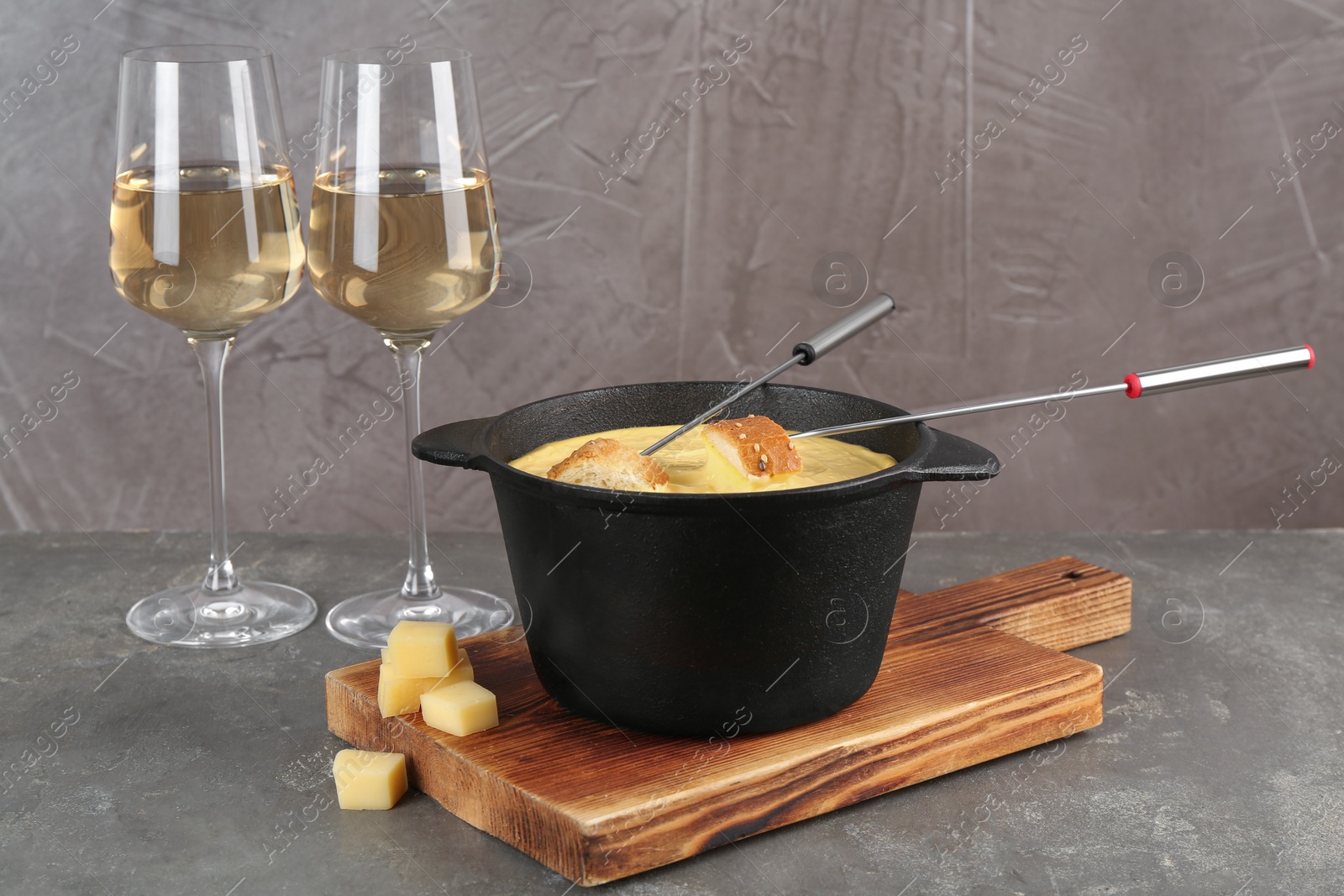 Photo of Fondue pot with tasty melted cheese, forks, bread and wine on grey table