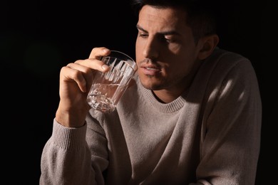 Addicted man with glass of alcoholic drink against black background, closeup