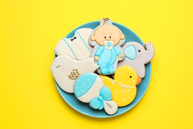 Plate of baby shower cookies on yellow background, top view