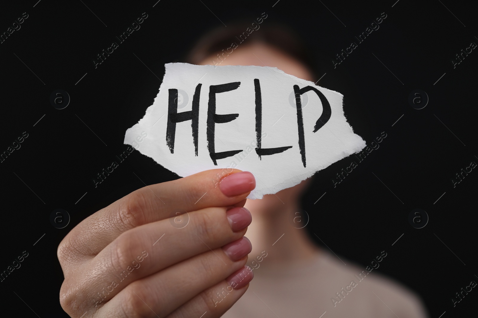 Photo of Woman holding piece of paper with word Help on black background, closeup. Domestic violence concept