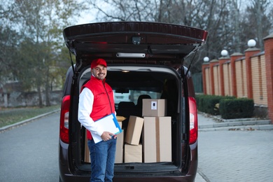 Deliveryman with clipboard near van with many parcels outdoors