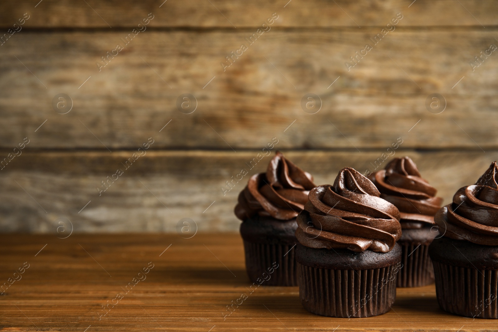 Photo of Delicious chocolate cupcakes with cream on wooden table. Space for text