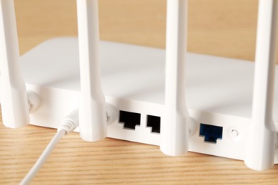 Photo of New white Wi-Fi router on wooden table, closeup