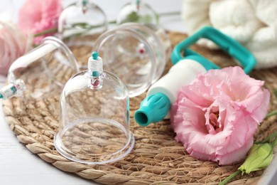 Photo of Plastic cups, hand pump and flowers on white table, closeup. Cupping therapy