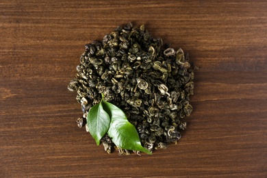 Photo of Heap of dried green tea leaves on wooden table, top view