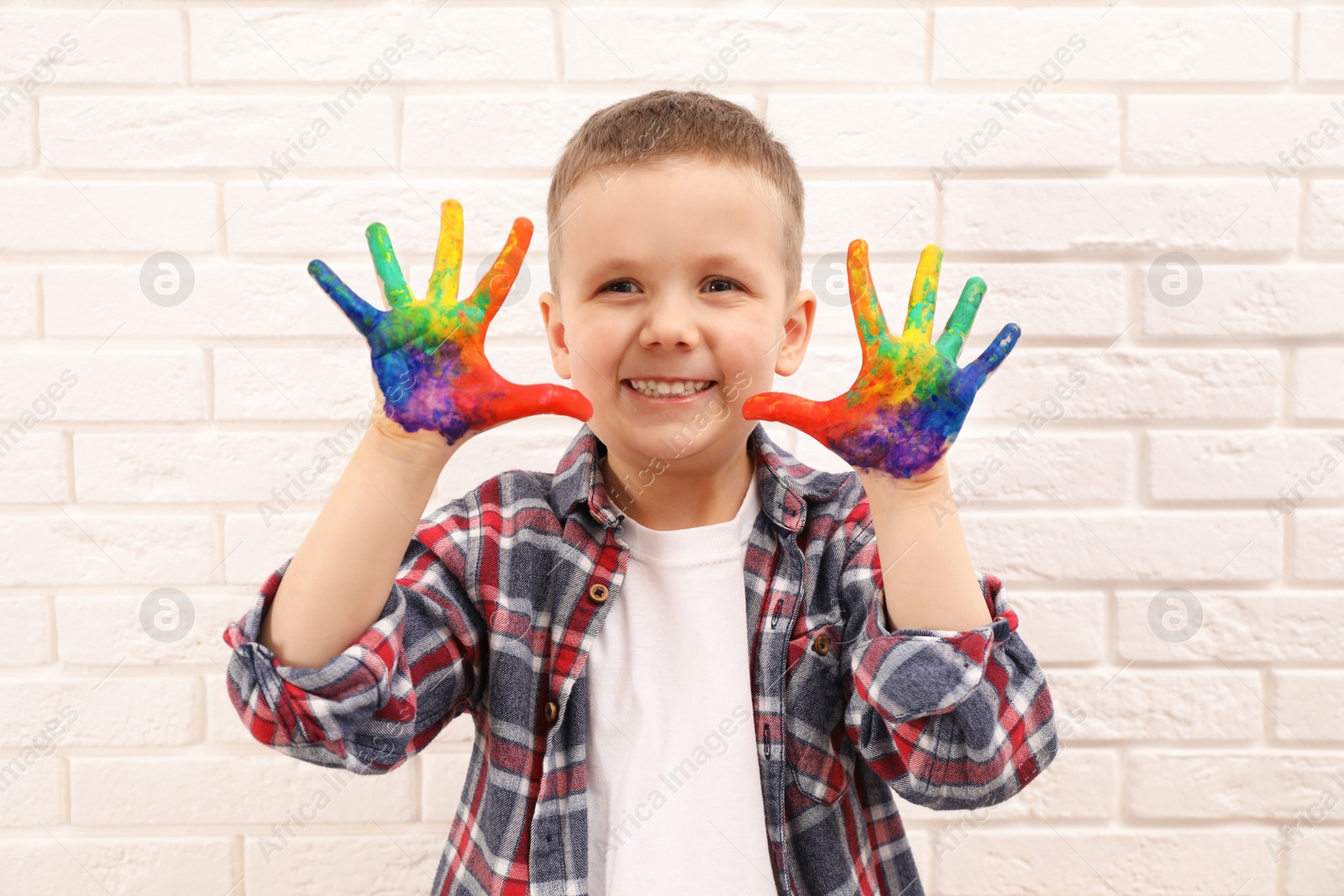 Photo of Happy little boy showing painted palms near white brick wall