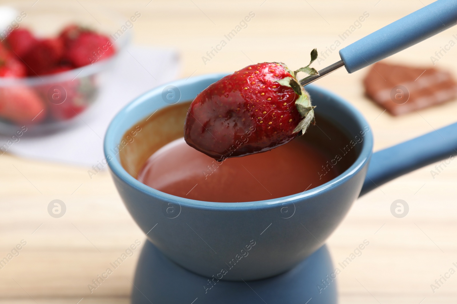 Photo of Dipping strawberry into pot with chocolate fondue on table, closeup