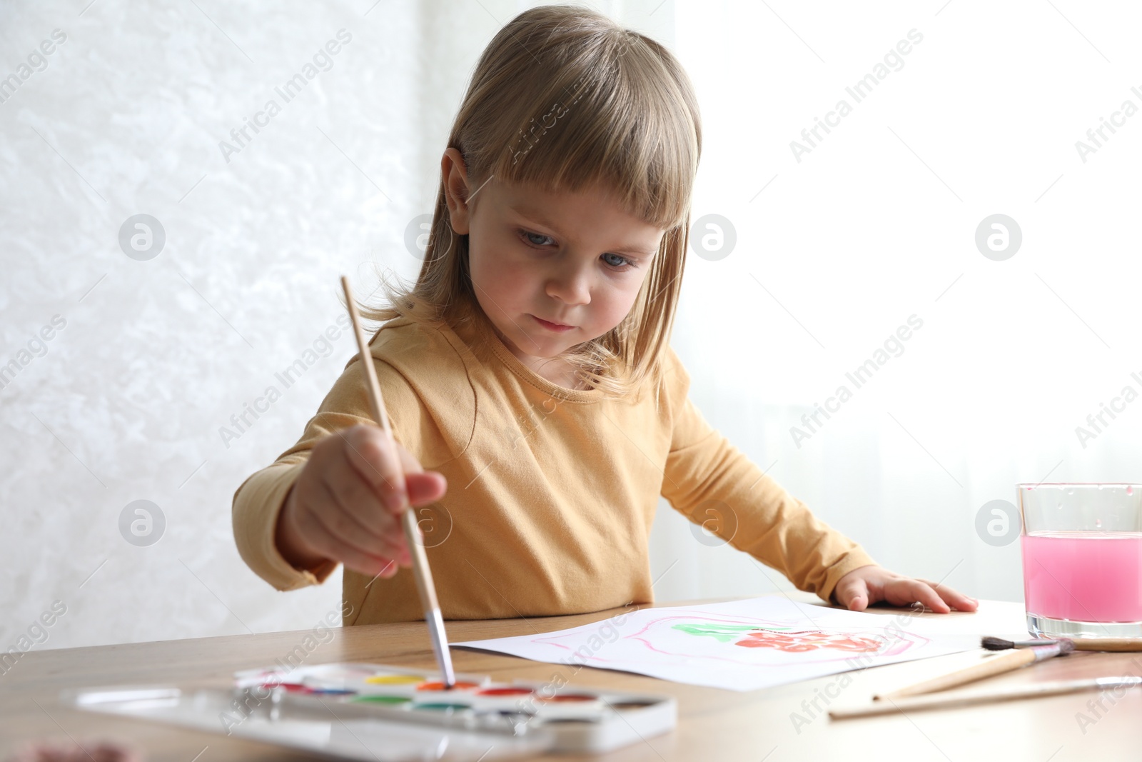 Photo of Cute little girl drawing with brush at wooden table indoors. Child`s art