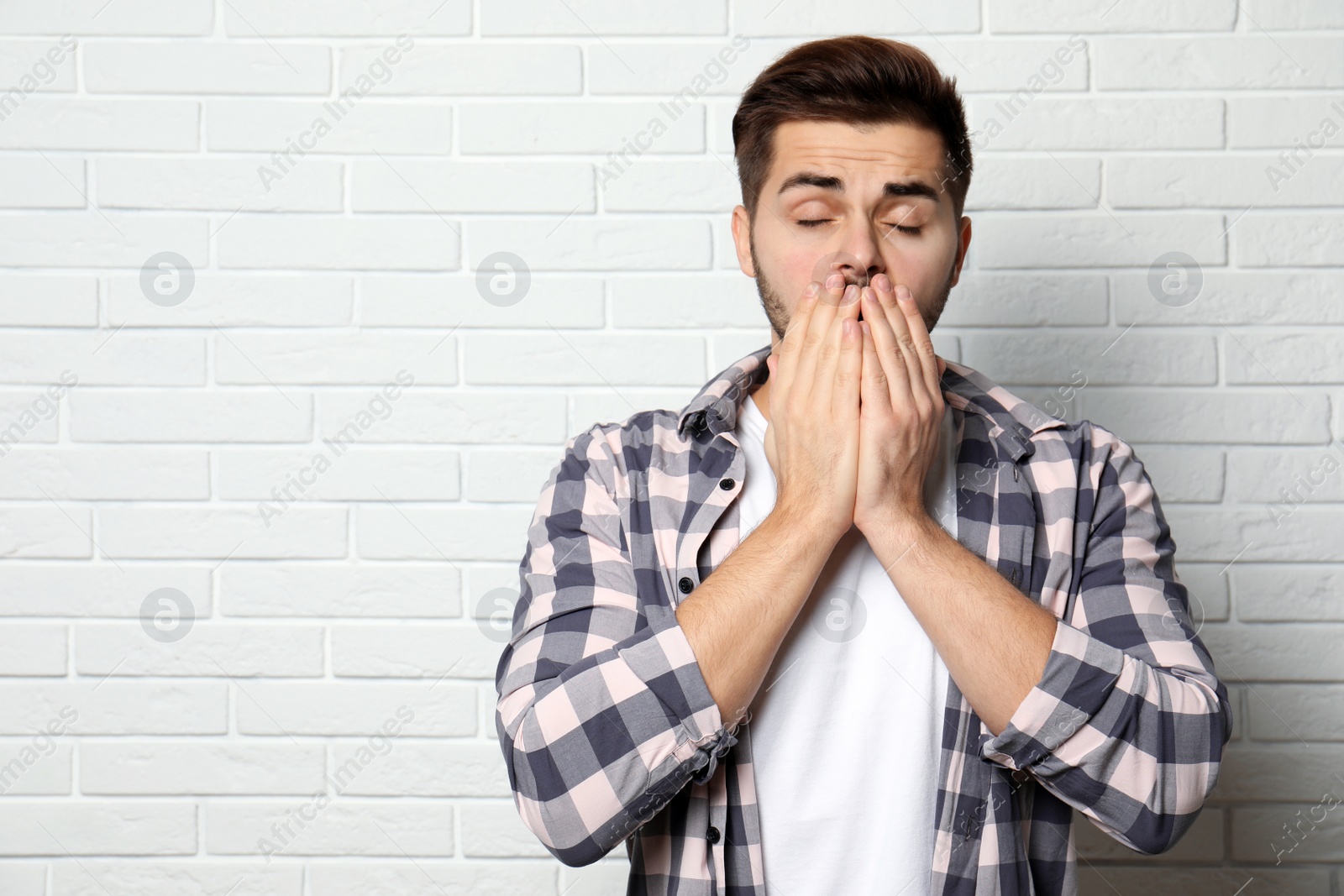 Photo of Handsome young man coughing near brick wall. Space for text
