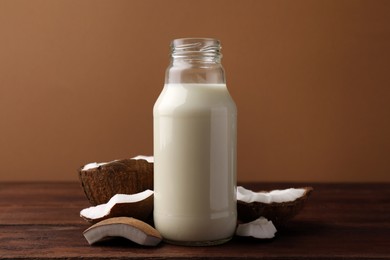 Photo of Bottle of delicious vegan milk and coconut pieces on wooden table