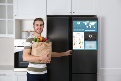 Image of Young man with bag of groceries near smart refrigerator in kitchen