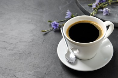 Photo of Cup of delicious chicory drink and flowers on black table. Space for text