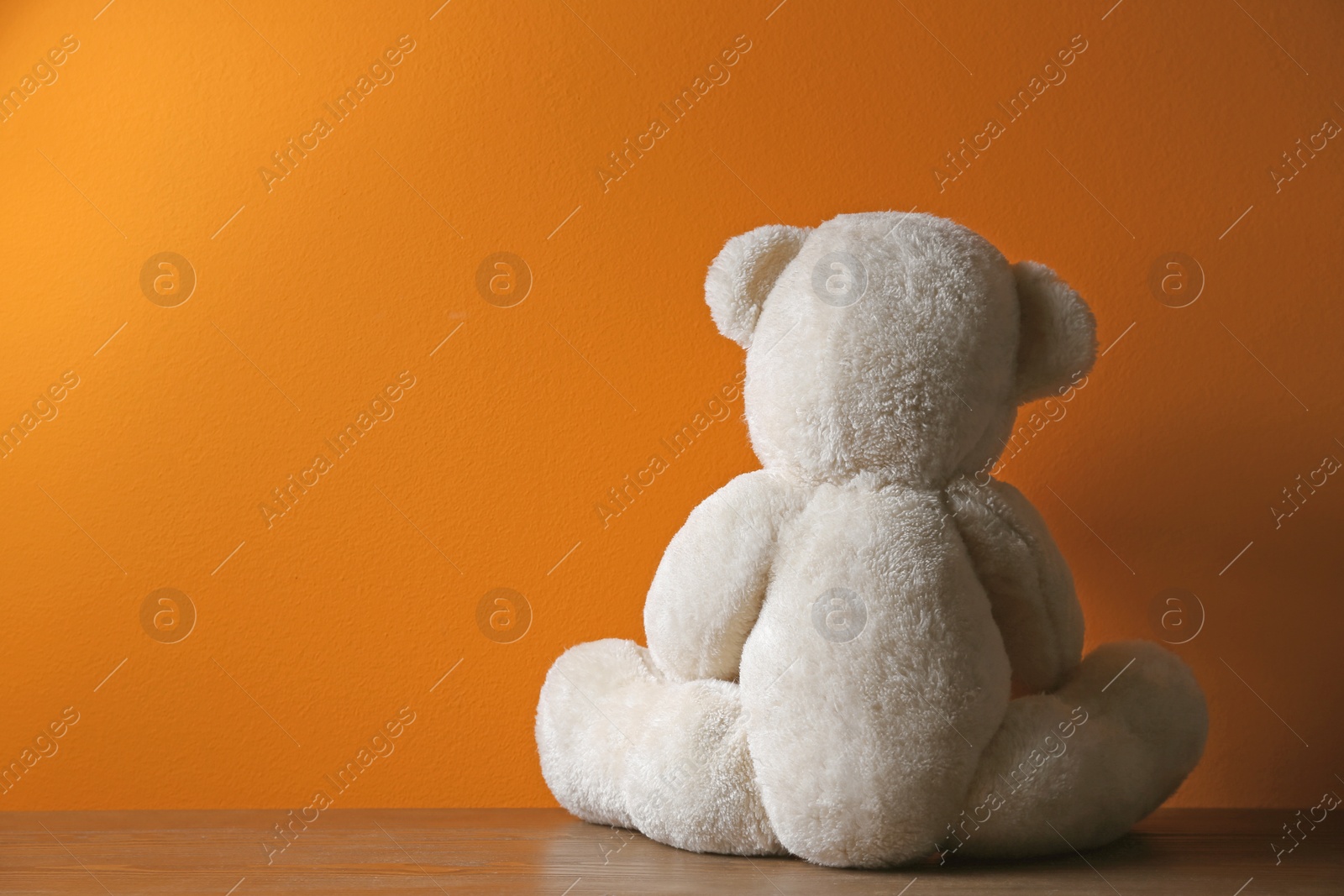 Photo of Abandoned teddy bear on table against color background. Time to visit child psychologist