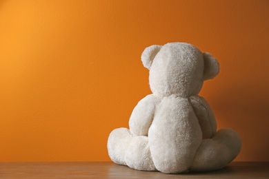 Photo of Abandoned teddy bear on table against color background. Time to visit child psychologist