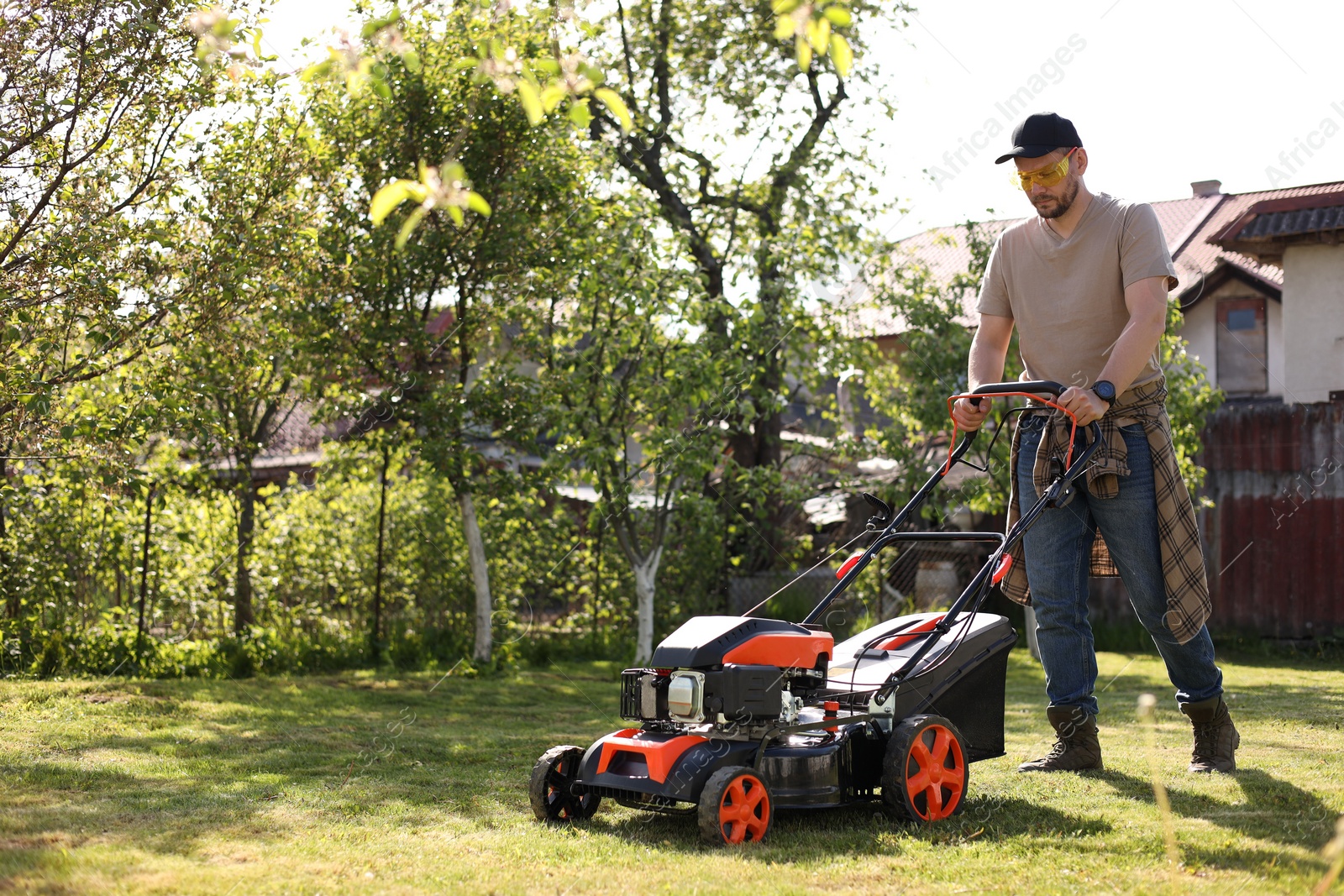 Photo of Man cutting green grass with lawn mower in garden