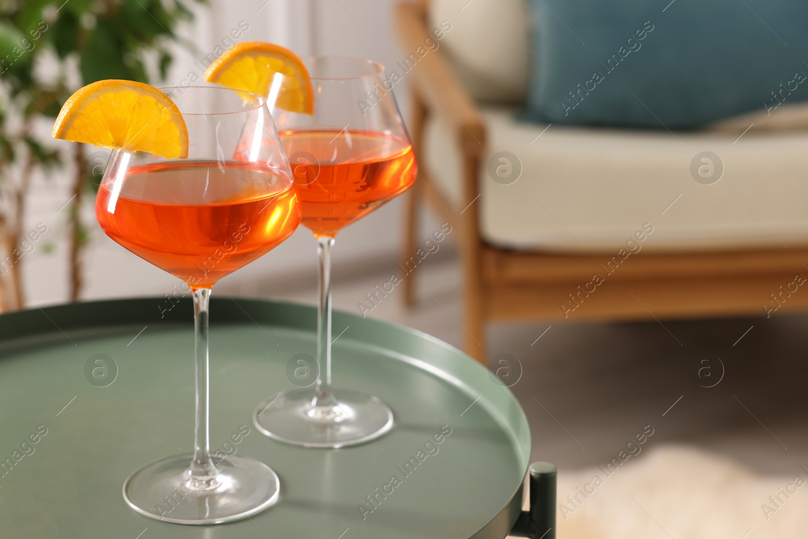 Photo of Tasty cocktail in glasses with orange slices on table in room, space for text. Relax at home