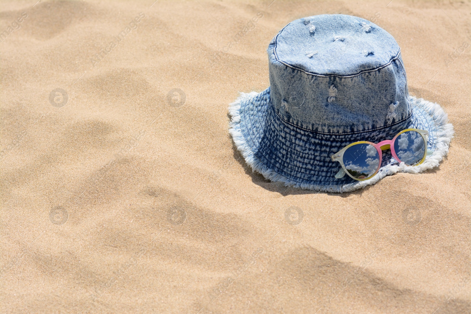 Photo of Jeans hat and sunglasses on sand, space for text. Beach accessories