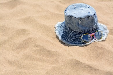 Photo of Jeans hat and sunglasses on sand, space for text. Beach accessories