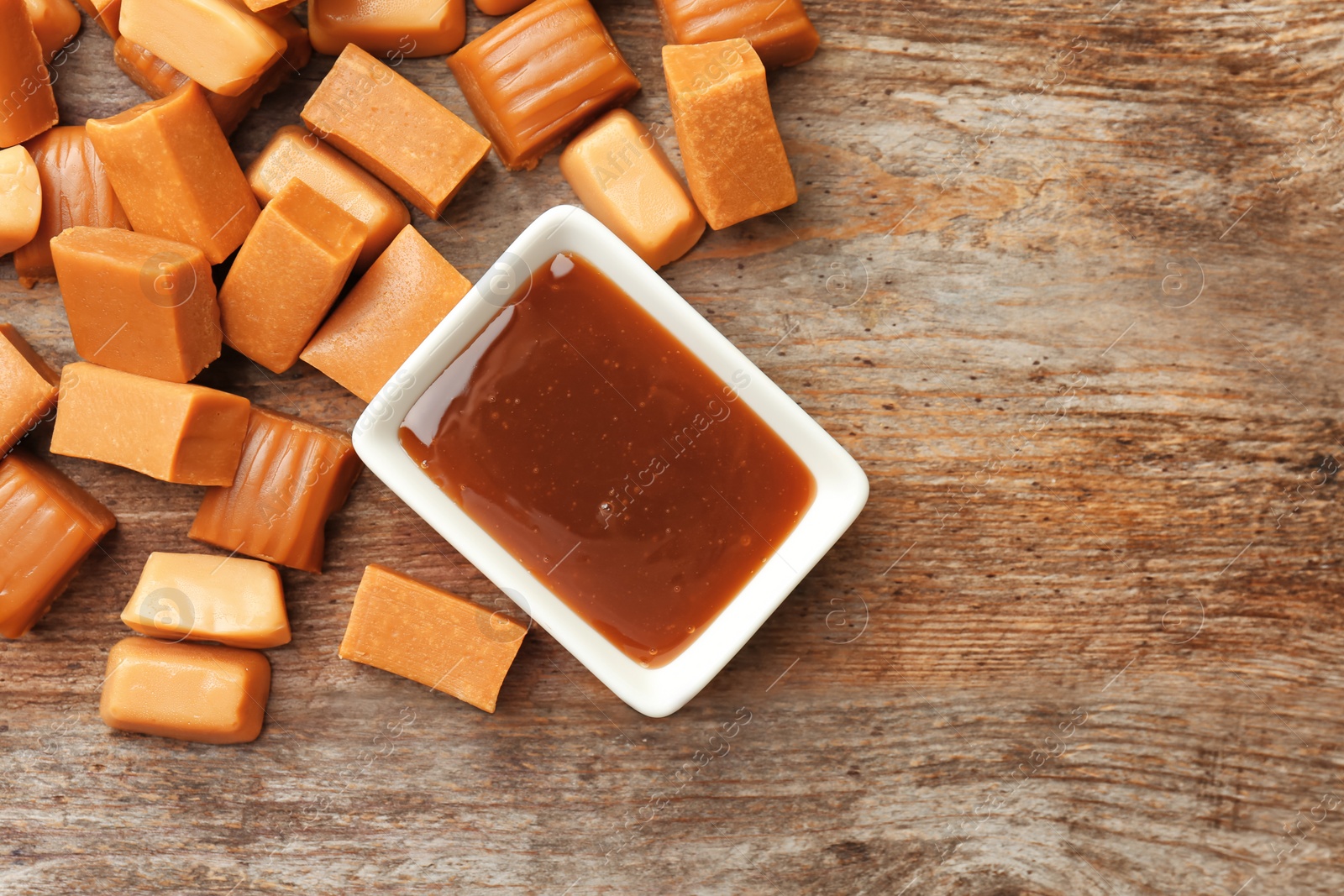 Photo of Delicious caramel candies and sauce on wooden background