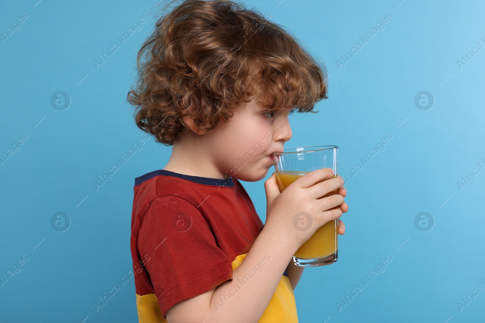 Photo of Cute little boy drinking fresh juice on light blue background