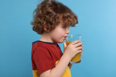 Cute little boy drinking fresh juice on light blue background