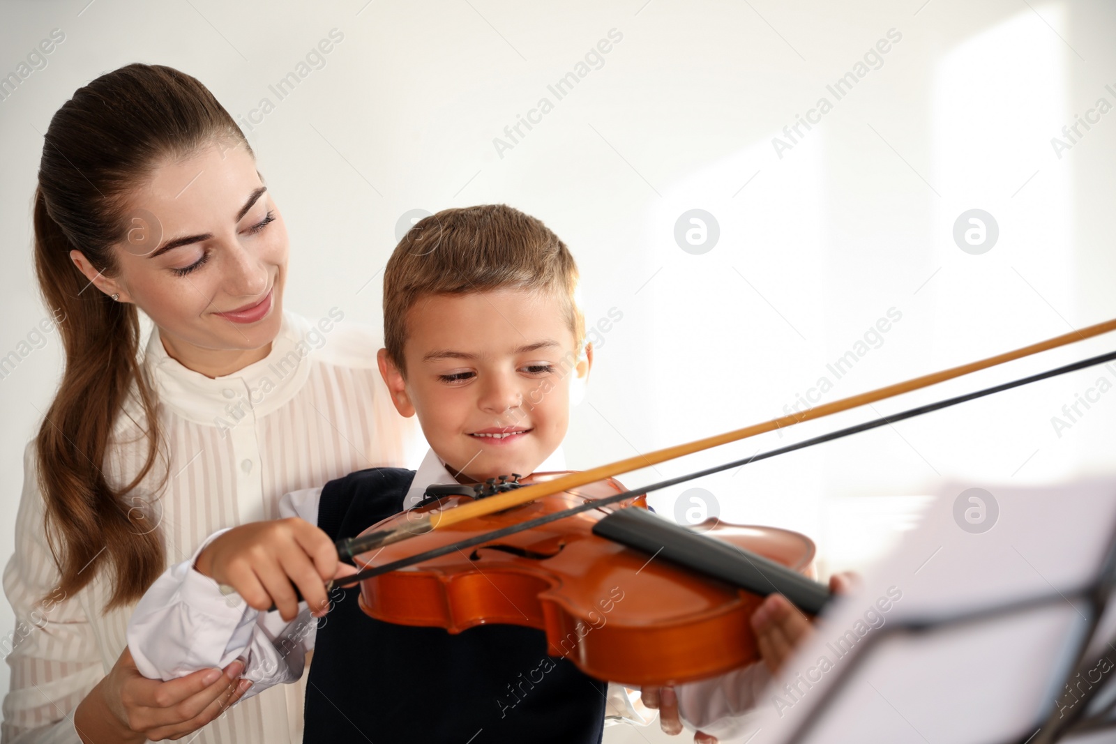 Photo of Young woman teaching little boy to play violin indoors