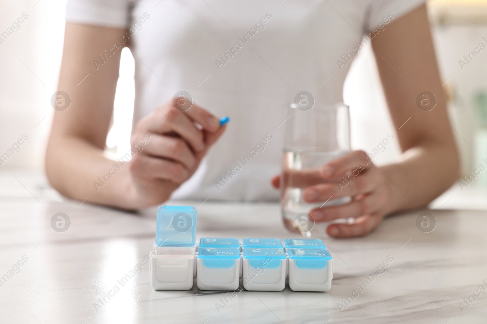 Photo of Woman with pills, organizer and glass of water at white marble table, selective focus