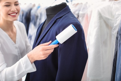 Photo of Young woman removing dust from jacket with lint roller at dry-cleaner's