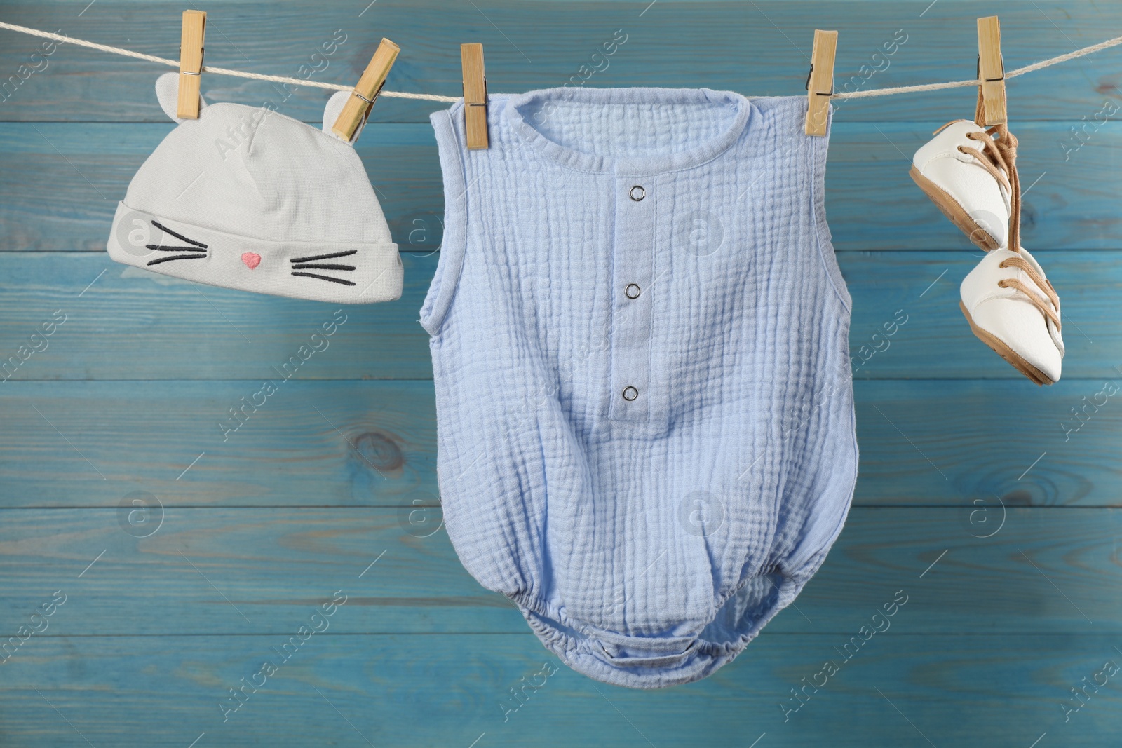 Photo of Baby clothes hanging on washing line near light blue wooden wall