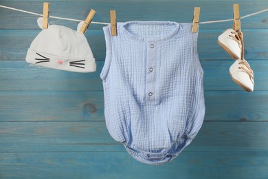 Baby clothes hanging on washing line near light blue wooden wall